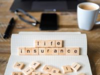 Closeup on notebook over wood table background, focus on wooden blocks with letters making Life Insurance words