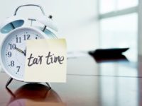 A clock with tax time sticky note and calculator on the desk